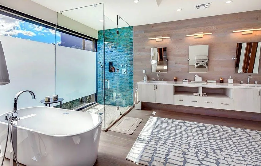 Whitewashed oak floating vanity with long bar pulls faces a freestanding soaking tub and a glass shower clad in turquoise glass mosaic, with wood-look plank walls and a picture window
