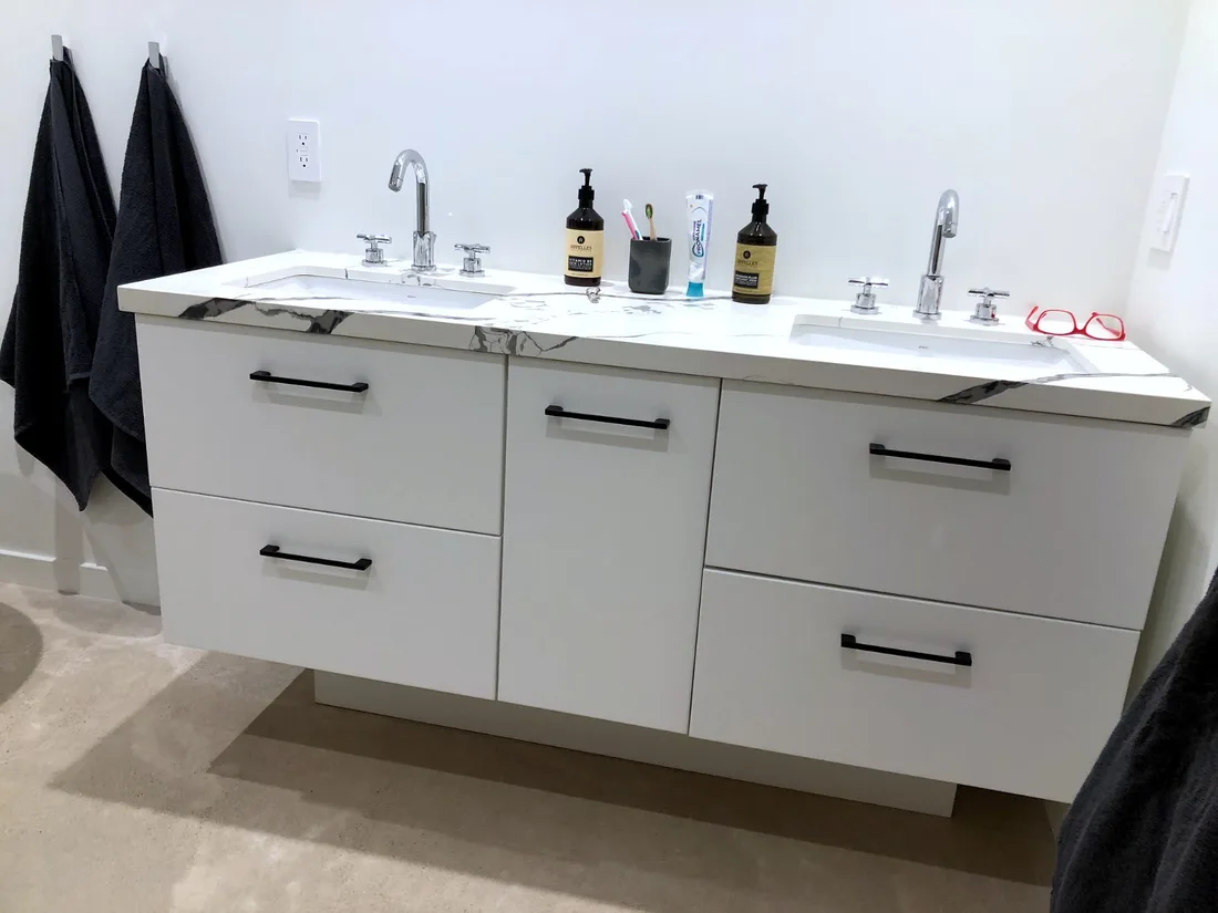 Floating white slab double vanity with matte black bar pulls, a dramatic black-and-white marble-look quartz top and twin undermount sinks against a crisp white wall
