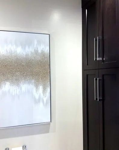 A tall espresso shaker cabinet with chrome bar pulls standing beside a framed gold-and-silver abstract canvas on a white wall — custom millwork hand-built by Classic Woodworking & Vanity in Hamilton, Ontario