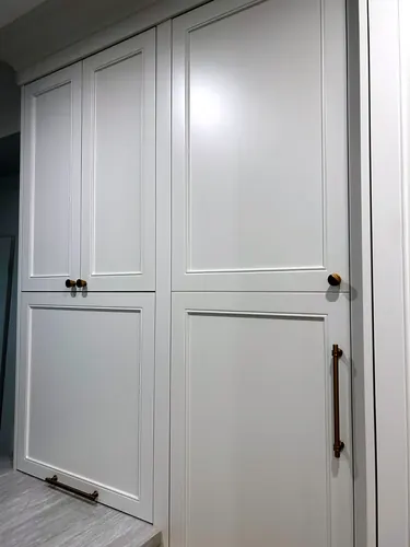 A wall of floor-to-ceiling sage-grey cabinetry with recessed inset-panel doors mixes antique brass round knobs and a long bar pull, set on a pale grey stone floor — custom millwork hand-built by Classic Woodworking & Vanity in Oakville, Ontario