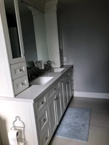 Grey raised-panel double vanity with a central mirrored storage tower, grey quartz countertop, twin undermount sinks and crystal-look knobs against a charcoal accent wall — custom vanity hand-built by Classic Woodworking & Vanity in Mississauga, Ontario