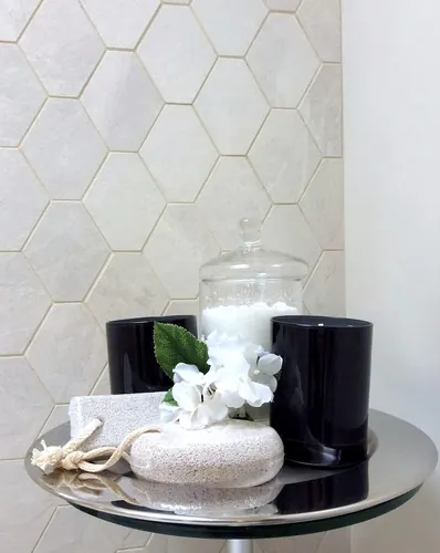 Styled bathroom vignette of black candle jars, a glass bath-salt canister and pumice stones on a chrome side table against a cream hexagon mosaic tile wall — custom other hand-built by Classic Woodworking & Vanity in Milton, Ontario