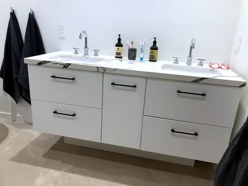 Floating white slab double vanity with matte black bar pulls, a dramatic black-and-white marble-look quartz top and twin undermount sinks against a crisp white wall