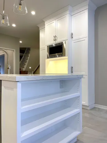 White shaker cabinetry with a built-in stainless microwave niche, glass pendant lights, marble-look quartz counter, and an open-shelf island end panel beside a staircase — custom kitchen hand-built by Classic Woodworking & Vanity in Vaughan, Ontario