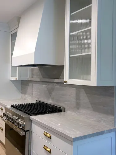 Sculpted white plaster-style range hood beside reeded fluted-glass cabinets with brass cup pulls, over a stainless gas cooktop and grey marble backsplash and counters — custom kitchen hand-built by Classic Woodworking & Vanity in Oakville, Ontario